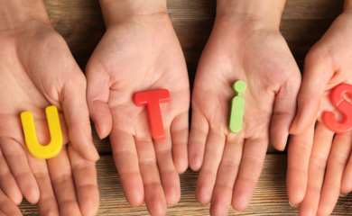 The image consists of 6 hands laid side by side. Each hand holds a plastic, brightly coloured, magnetic letter. Together the letters spell autism.