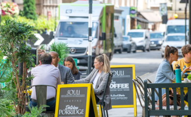 Diners seated at tables outside a cafe, immersed in conversation on a vibrant and busy city street.