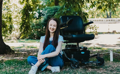 A photo of Pippa sat in a park next to her power chair.