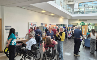 A small crowd of people in a hospital foyer for a networking event with people talking,smiling and roller banners in background. 