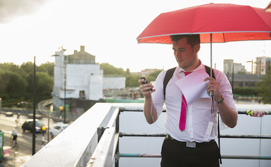 Man holding a red umbrella, looking at a smartphone screen