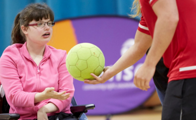 Girl with brown hair and glasses sitting in wheelchair in a sports hall