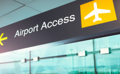 A black and yellow airport sign with the words 'Airport Access' and a yellow arrow pointing to the left. There is a yellow and white airplane graphic to the right. 