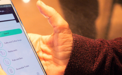 A hand holding a Samsung phone with the AccessAble App on screen.