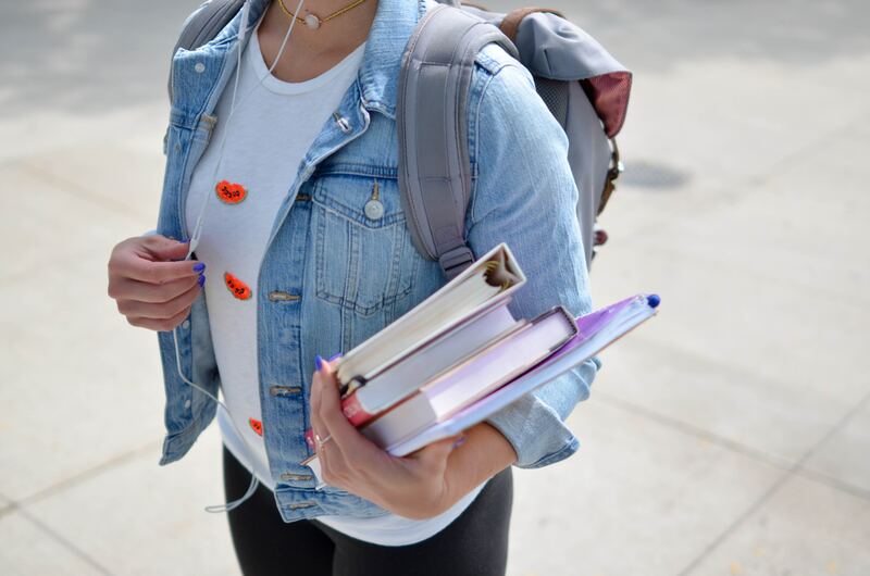 a university student wearing a denim jacket and backpack, wearing headphones and carrying a stack of books