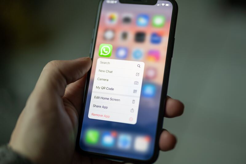 a hand holding a phone, with the green WhatsApp app selected and showing the option to search or start a new chat