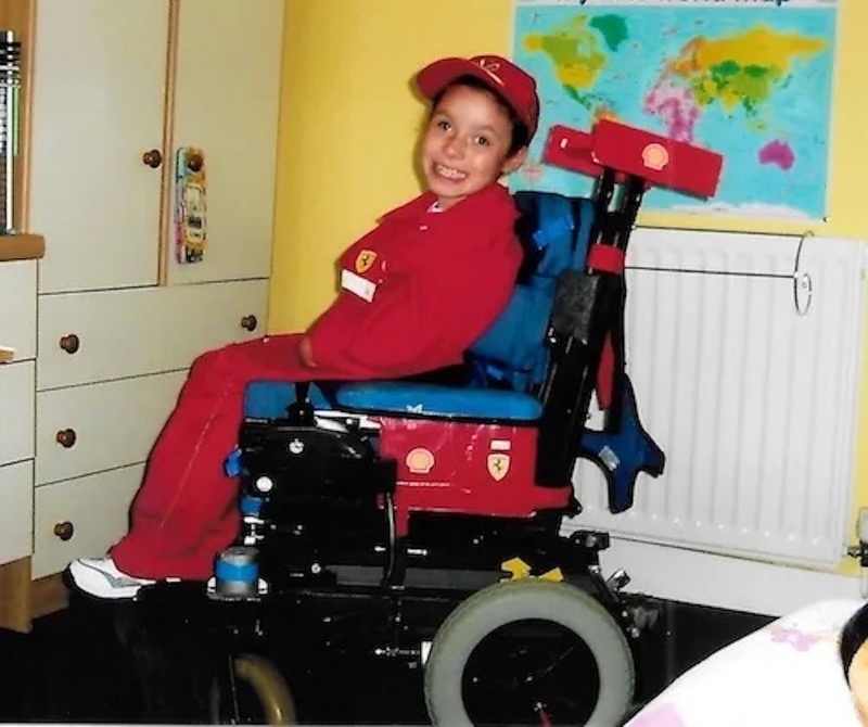 Emma Purcell as a child, dressed up as the F1 driver Michael Schumacher for Sport Relief. She's wearing a red cap and tracksuit, and has made her wheelchair into a red racing car.