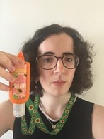 Lydia, a white women with brown hair and glasses, wearing a sunflower lanyard and holding a bottle of hand sanitiser