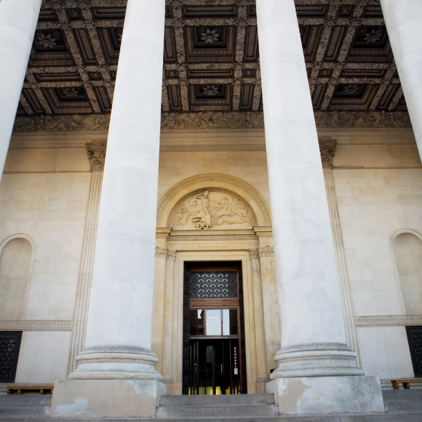 Image shows the exterior of the Fitzwilliam Museum. There is four pillars in front of the door in the middle of the building.