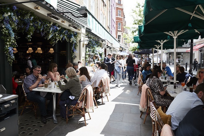 Photo of people eating outside at restaurants, there are canopies above the outdoor seating areas.
