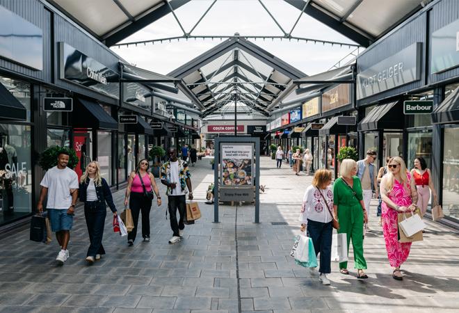 "Covered outdoor shopping walkway with designer stores, signage, and people carrying shopping bags"