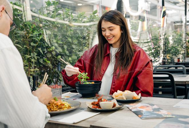 "Two people dining at an outdoor restaurant table with plates of noodles, dumplings, and drinks"