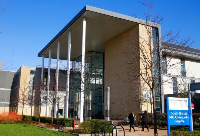 The front of the South Bristol Community Hospital building, the entrance is a tall, half brick half glass building with a large overhanging roof held up by 5 large white pillars. 