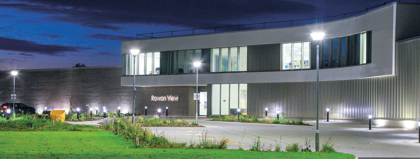 "Front of Rowan View Hospital at night with lighting on lampposts and bollards outside"