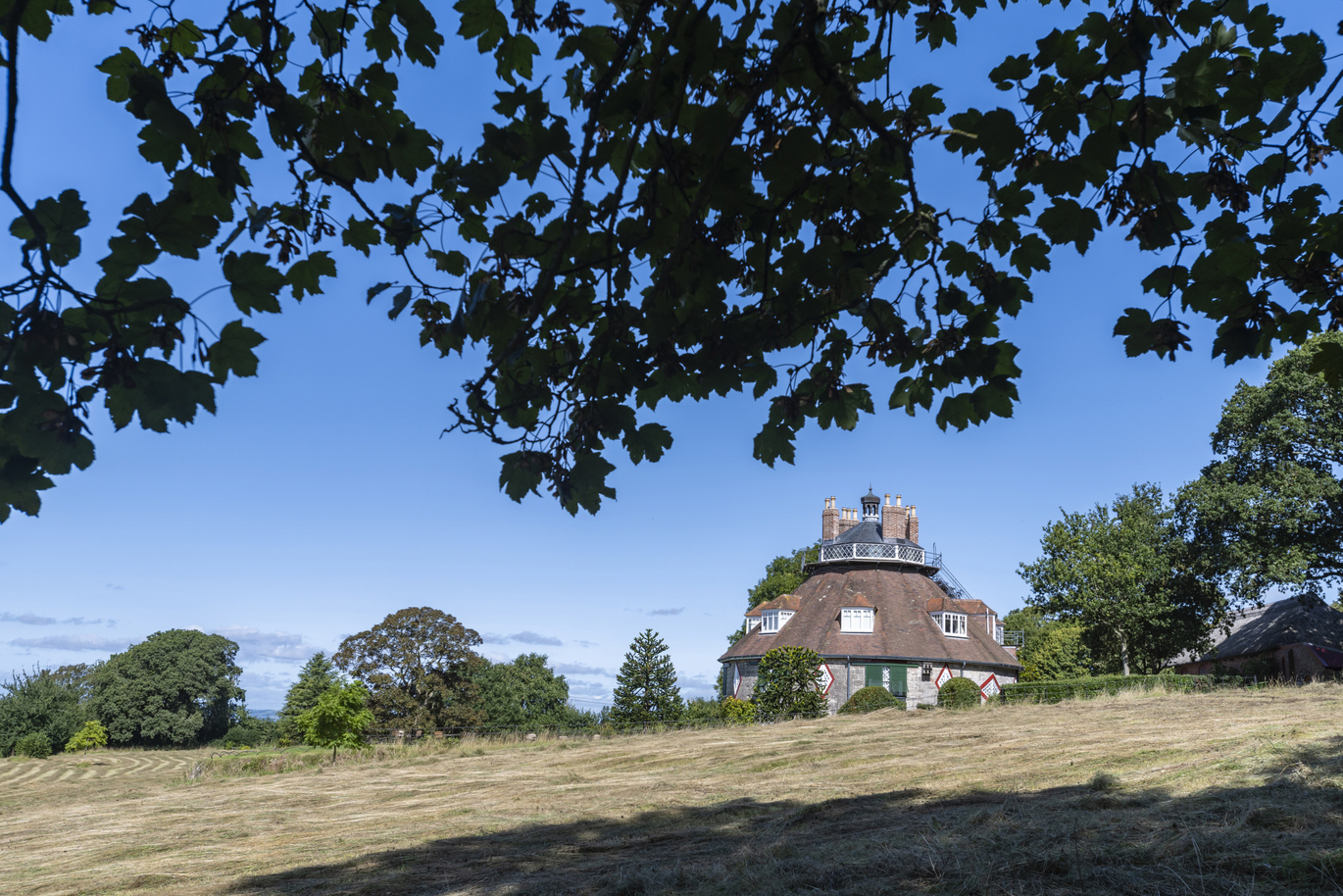 A view through the fields, under the trees of the exterior of the 16 sided, 18th century house.