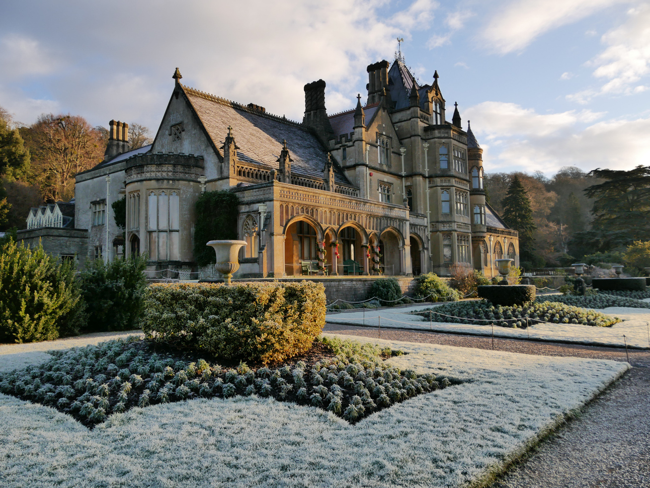 The large medieval type house and gardens with stone paths around squares of grass with neatly trimmed hedges in frost.