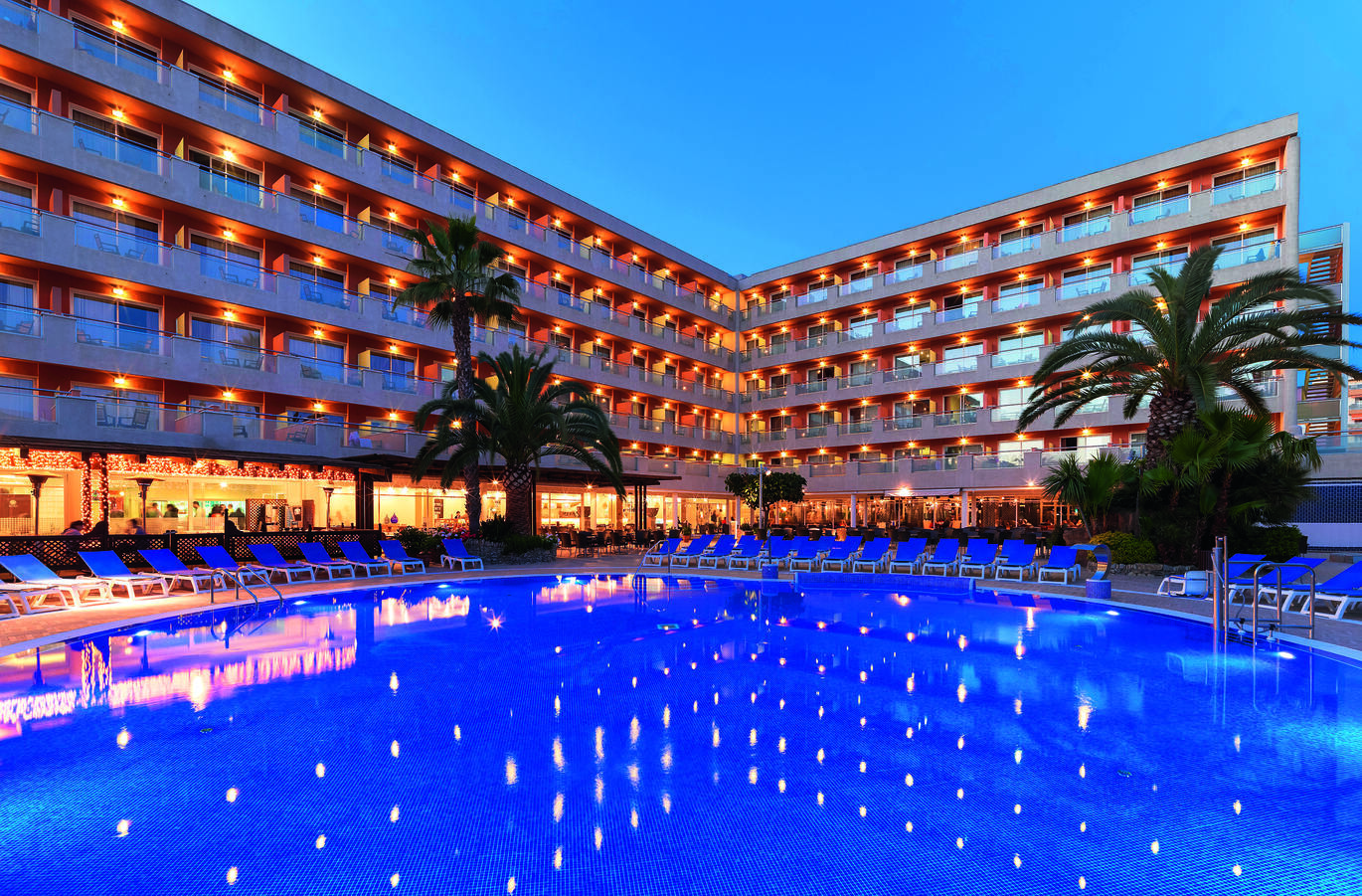 View from the pool of the tall hotel building behind all lit up in the evening, reflecting in the pool.