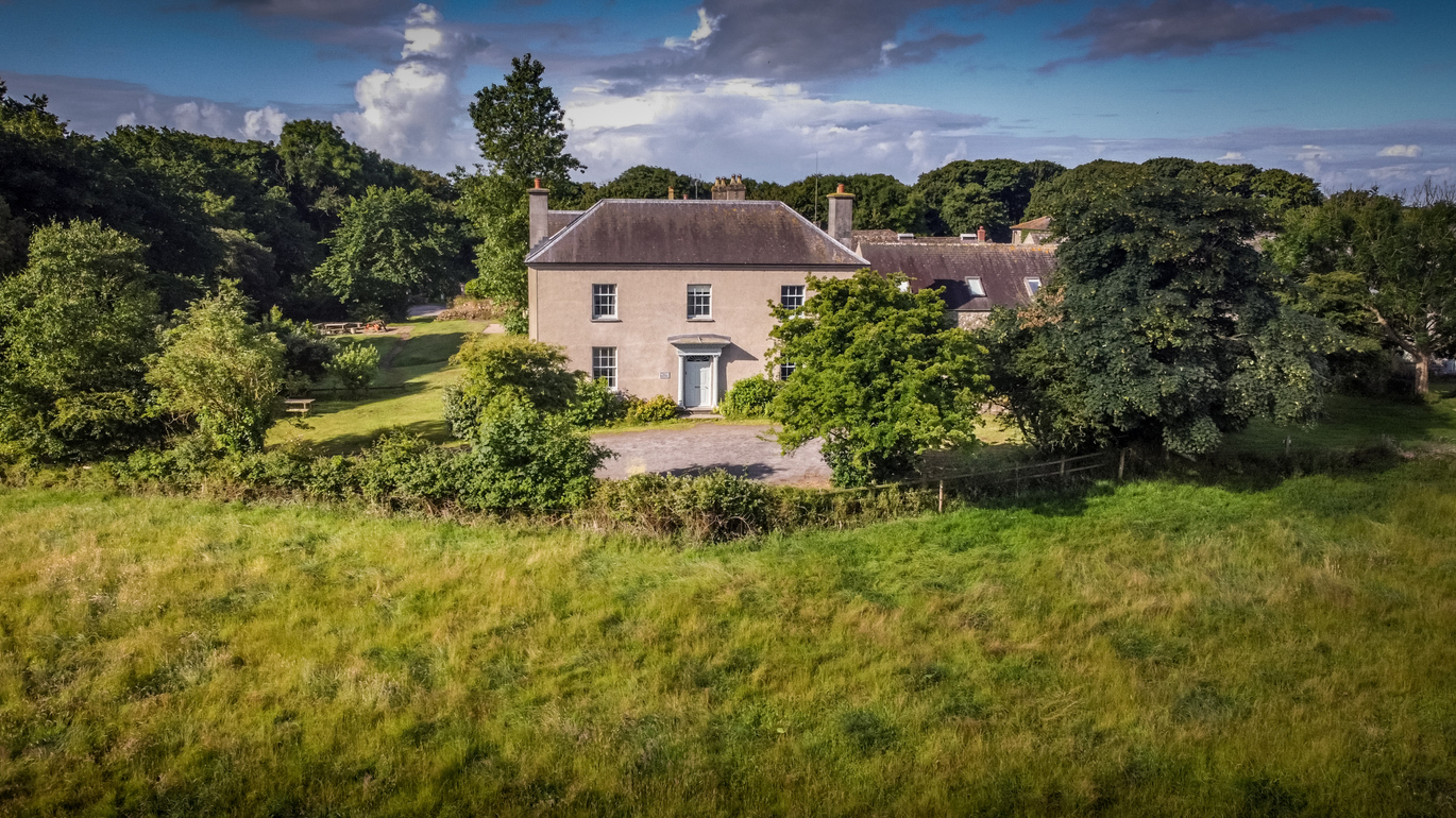 The exterior of Stackpole Manor on a sunny day surrounded by lots of green lawn and many, many trees.