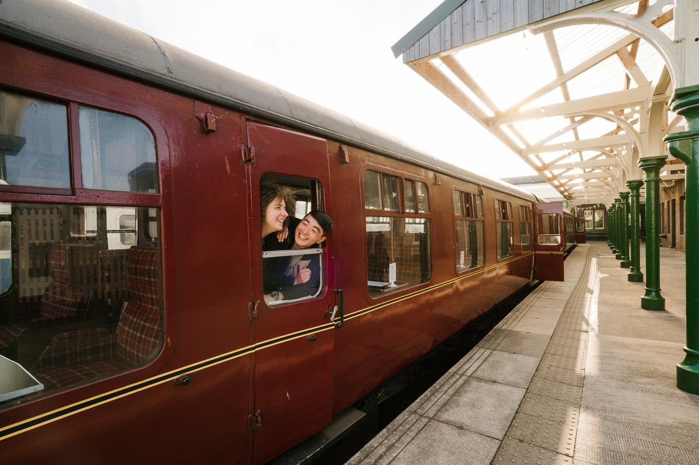 "A man and a woman looking out of a window from inside of a train at Caledonian Railway, Brechin Station in Angus, Scotland."