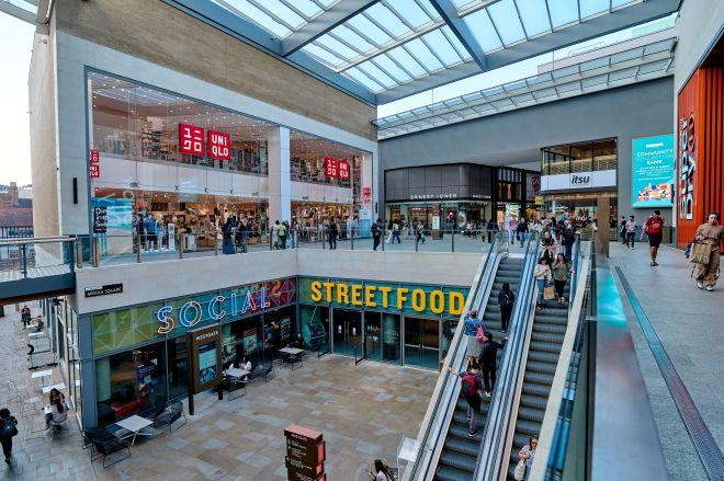 "Indoor shopping centre at Westgate with escalators, shops and people moving between levels."