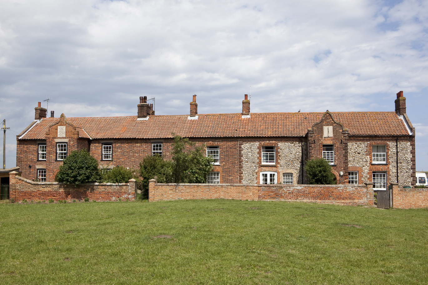 View of the front of the 17th century Brancaster Millennium Activity Centre with a small wall around leading onto a green lawn.