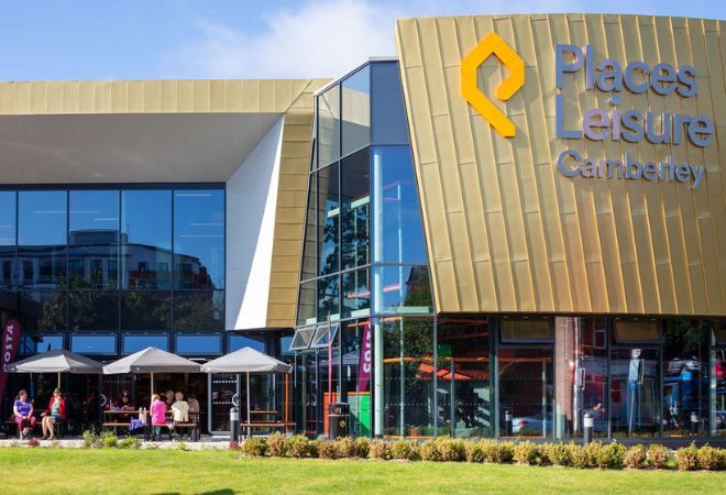''Camberley leisure centre from the outside. people sitting outside on benches, covered with umbrellas''
