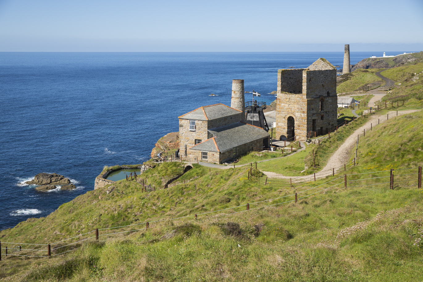 A view of Michell's engine house at Levant Mine, in a grassy field on top of a cliff directly above the sea.
