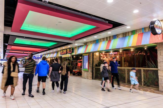 "Indoor walkway at Xscape with visitors walking past an entertainment venue with colourful striped frontage."
