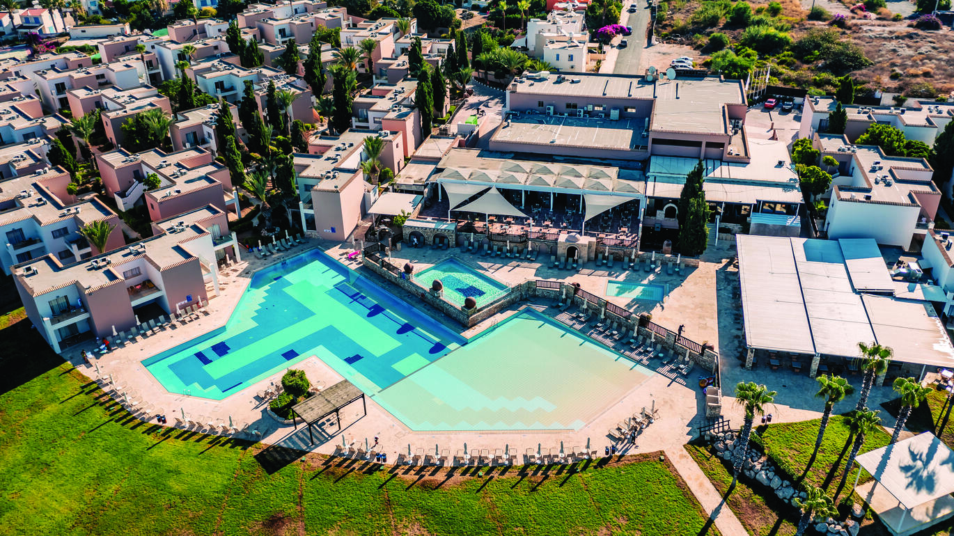 Aerial view of the many small apartment buildings with the large pool at the front and a lawn in front of the pool.