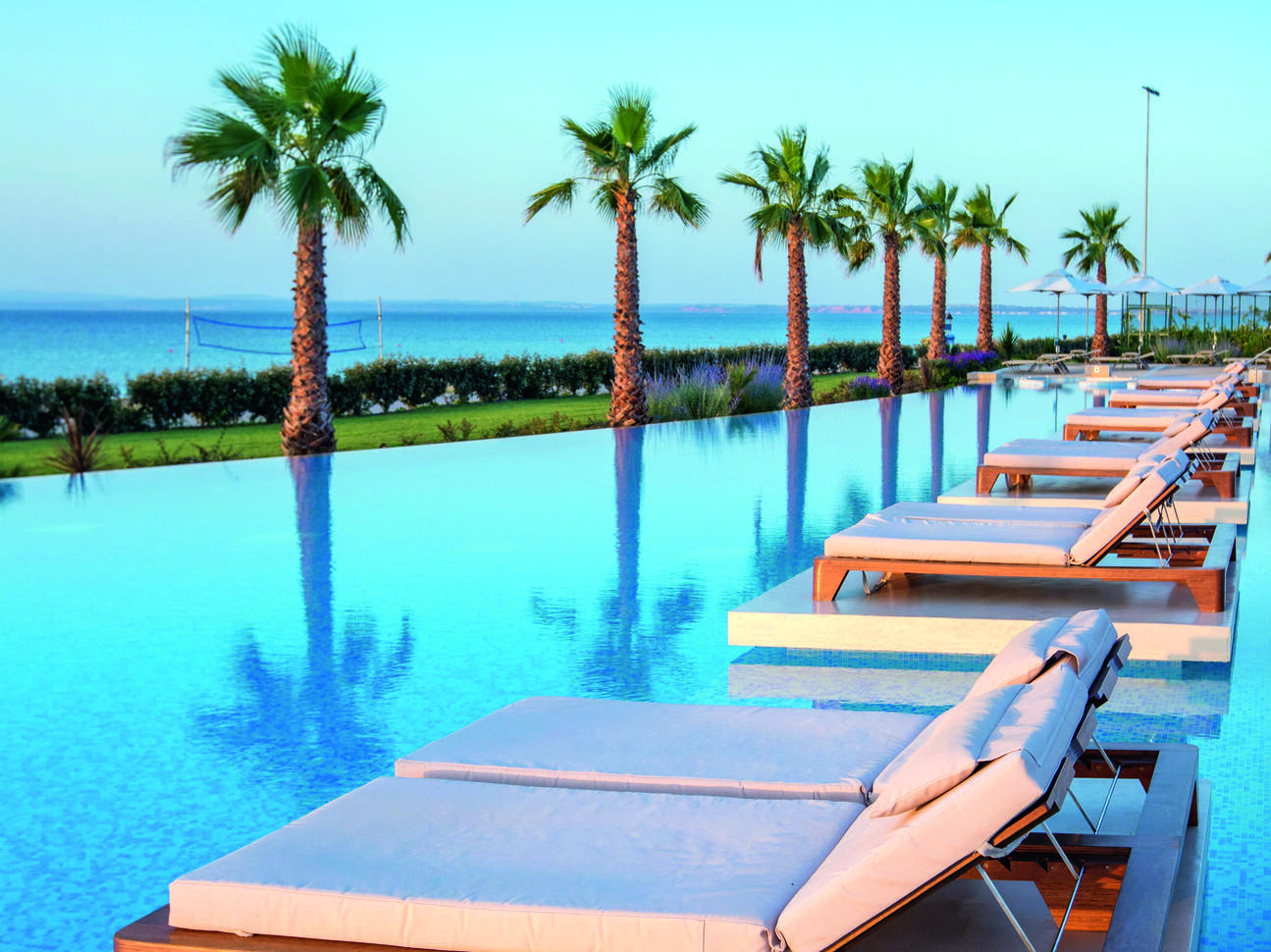 Sun beds in the pool looking through the palm trees into the sea with the blue sky above.