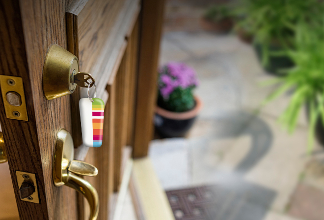 "a door is ajar, with keys in the door, and a sequence keyring hanging from them. "