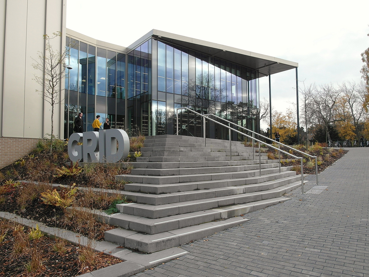 "Glass front building with steps in foreground, GRID sign to left and white sky in background"