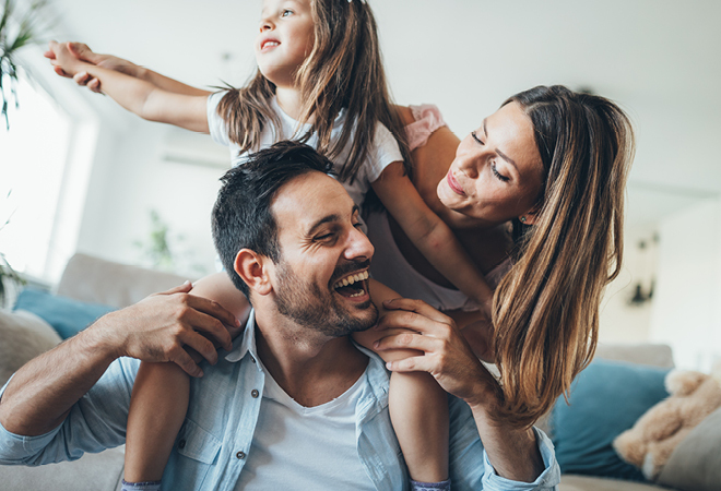 A family smiling and playing, the child is sat on her fathers shoulders
