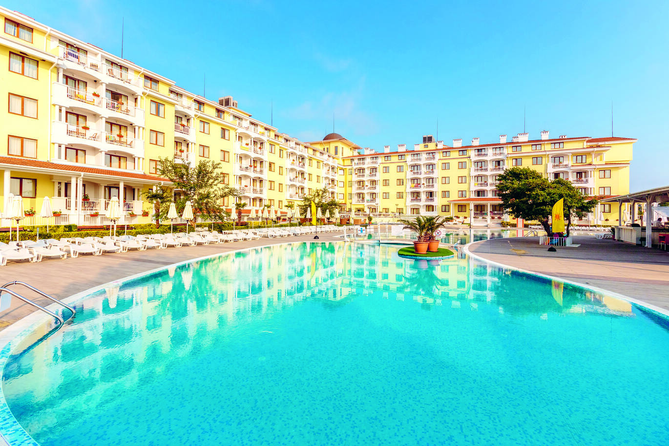 View of the large hotel building with the pool in front surrounded by seating and umbrellas.