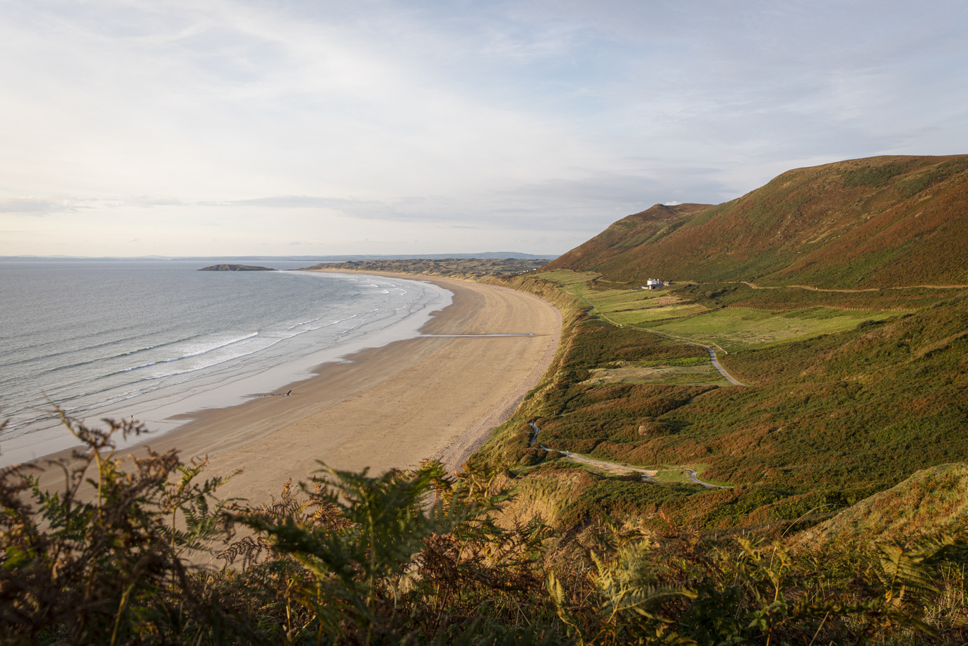 The historic Rhossili Old Rectory holiday cottage, the only building on the world-famous Rhossili Bay at Rhosili and South Gower Coast, Swansea, with steep hills directly behind and a small cliff in front with the beach and sea directly below.
