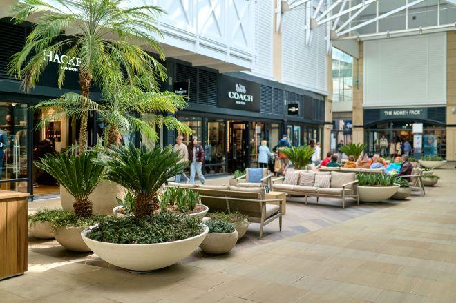 "Indoor outlet shopping area with seating, plants and premium stores including Coach and The North Face."