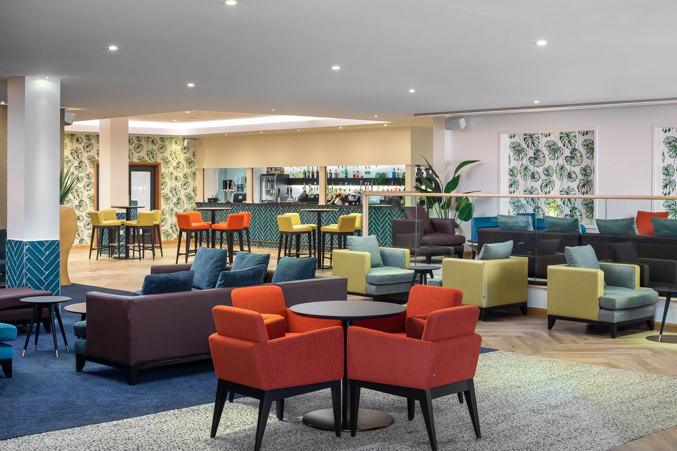 "Open plan space with several seating areas of sofas and armchairs with coffee tables, further back there are high seats with small tables and a bar area."