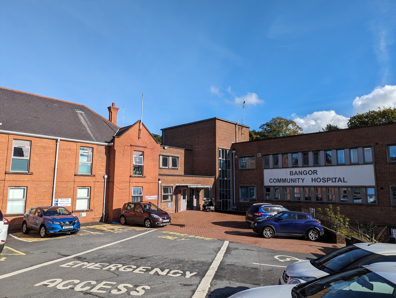 "External shot of Bangor Community Hospital. It is a red brick, two storey building with a car park near the main entrance."