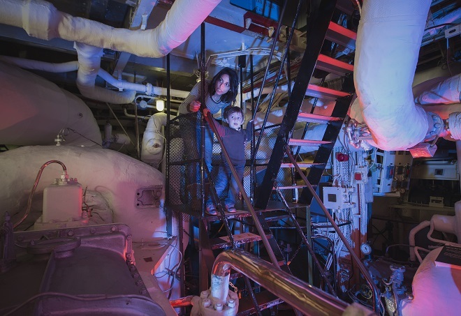 An adult and child going down the stairs inside part of HMS Belfast