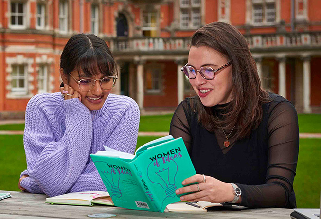 Two female students reading a book called 'Women of Ideas'