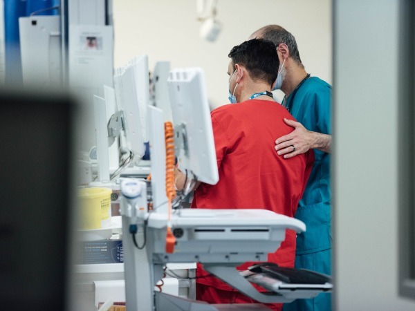 "Nurse caring for a patient at their bedside seen from the back"