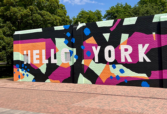 "Exterior image of a wall with modern style brightly coloured graffiti and the words 'Hello York'"