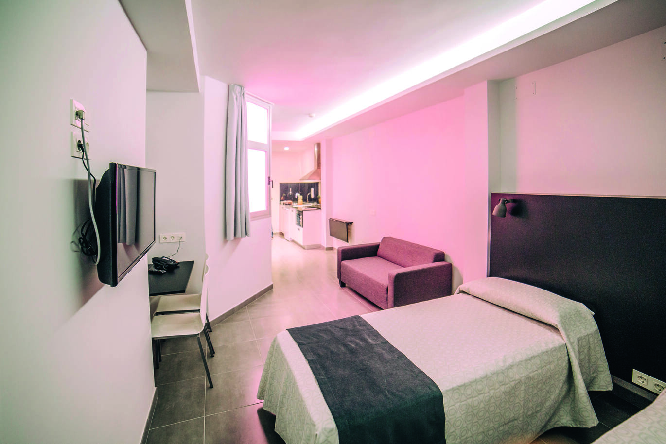 Inside an apartment showing beds, TV, sofa and kitchen.