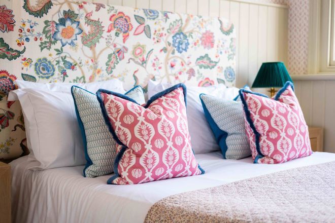 "Image of a bedroom at The Crown showing a double bed with white bedsheets and blue and pink cushions"