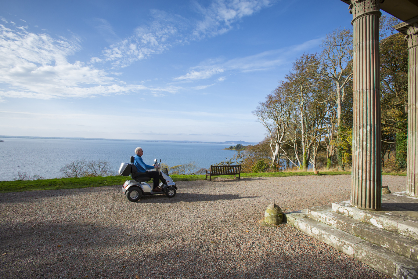 A visitor on a mobility scooter with a view of Strangford Lough behind, from the front of Mount Stewart.