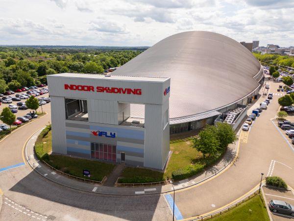 "iFLY indoor skydiving building at Xscape Milton Keynes with large curved dome and surrounding car park."