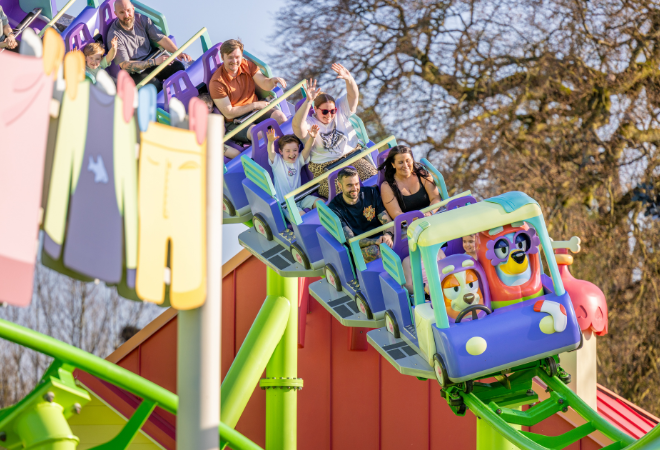"Family-friendly rollercoaster with colourful cartoon-themed carriage descending a track, riders raising hands."