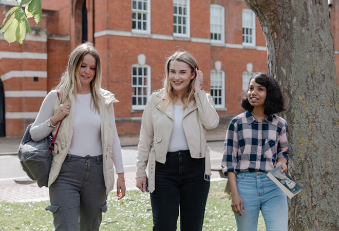"Image of three students walking outside next to a tree in front of a CCCU building"