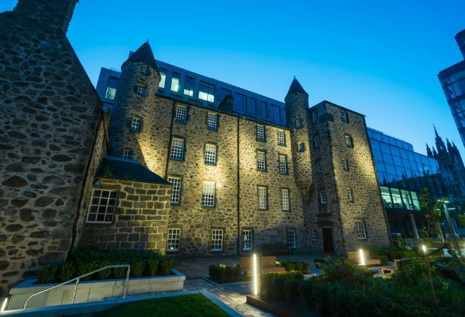 "Provost Skene House. Old large building with turrets and modern glass buildings to right side set against clear dusk sky."