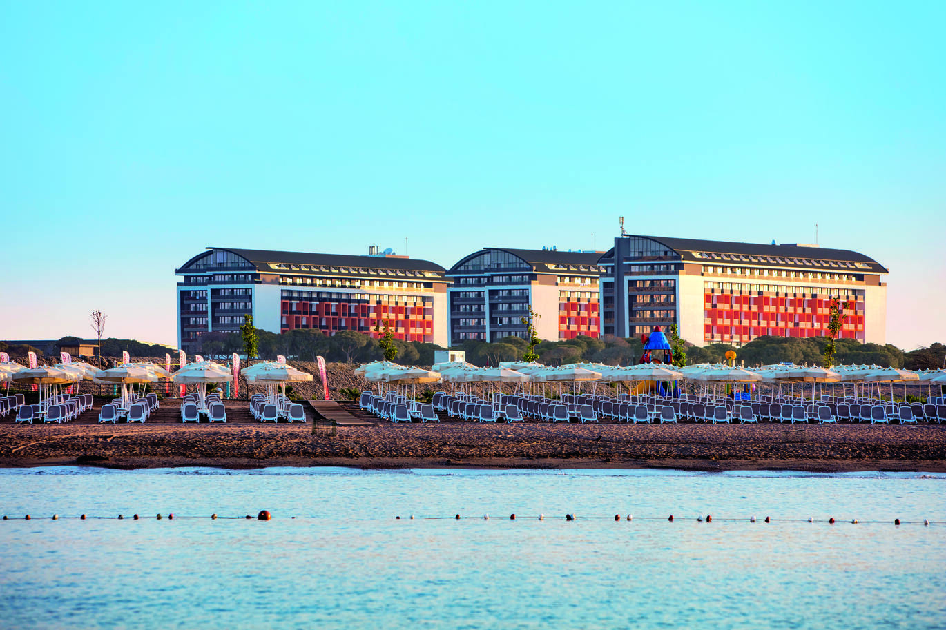 View from across the sea of the beach covered with sun loungers and umbrellas with the hotel buildings behind.